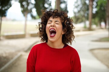 Young beautiful Arab woman standing outdoors wearing red sweater angry and mad screaming frustrated...