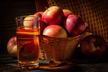 Basket with red apples and glass of apple juice on a dark wooden background