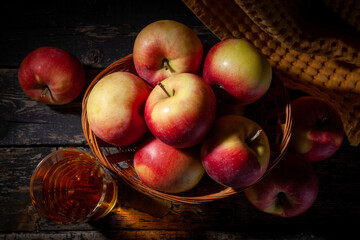 Basket with red apples and glass of apple juice on a dark wooden background