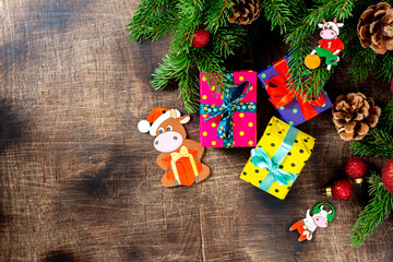Christmas background with gift boxes Packed in different colors on a brown wooden table. Christmas background with fir branches is decorated with the symbol of 2021 bull cow made of wood. Top view