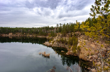 View of the lake with rocky shores and pines and cloudy sky, quarry, landscape. Natural background