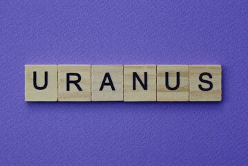 gray word uranus in small square wooden letters with black font on a lilac background