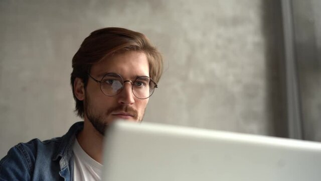 Smiling businessman working on laptop computer at home office. Male professional typing on laptop keyboard at workplace. Portrait of positive business man looking at laptop screen indoors