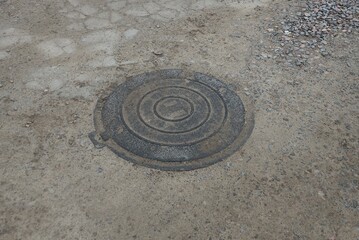 one black iron manhole lying on gray sand and concrete outside