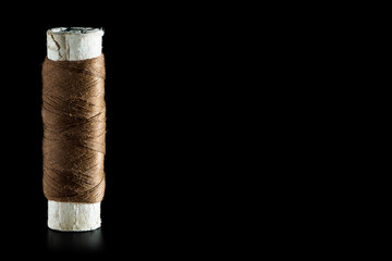 Reel with brown sewing silk threads isolated on a black background, close-up, copy space. Bright background for sewing and needlework