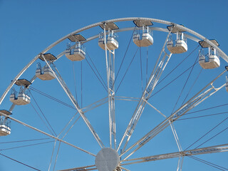 White ferris wheel with empty gondolas and blue sky