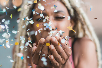 Happy african girl blowing confetti outdoor - Party concept - Soft focus on hands