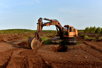 Excavator digging drainage ditch in peat extraction site. Drainage of peat bogs and destruction of...