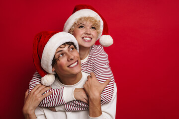 Young cheerful couple in Santa Claus hats smiling while piggyback riding