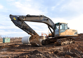 Excavator during earthmoving at construction site. Backhoe dig ground for the construction of foundation and laying sewer pipes district heating. Earth-moving heavy equipment on road works
