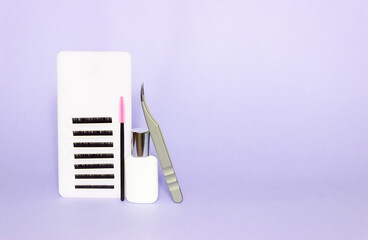 Fototapeta na wymiar Tablet with artificial eyelashes, brush, glue and tweezers for eyelash extension. Tools for the lashmaker. Purple background, levitation. Free space for text.