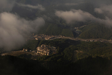 Fototapeta premium view from the top of the mountain through the clouds to the valley in the sunlight