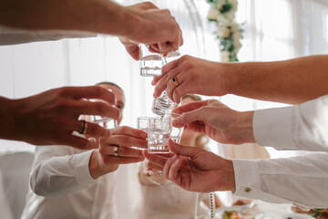 Hands holding the glasses of vodka and making a toast. The party, wedding, celebration, alcohol, lifestyle, friendship, holiday, christmas, new, year and clinking concept.