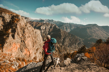 Hiker man with backpack standing on edge of cliff and looking at the mountains