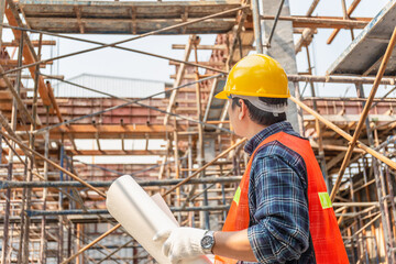 Worker man in hard hat holding blueprint checking and planning project at construction site