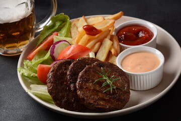 Burger meat steaks french fries and salad on black background
