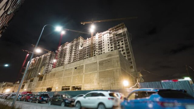 Beautiful motion timelapse of the construction works on a new skyscraper on the night. Camera moving towards the building with bare walls and giant cranes working in the light of lamps.