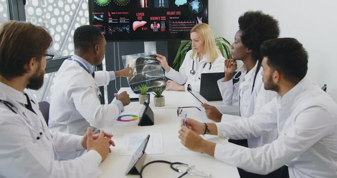 Medical concept where confident high-skilled likable international team of doctors discussing reasultsof patient's x-ray image and choosing the methods of treatment