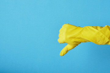 a hand in a yellow household rubber glove shows a thumb down on a blue background copy space....