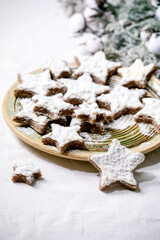 Homemade star shape cocoa almond cookies with white glaze and icing sugar. On ceramic plate with green branches decorations over white tablecloth. Copy space