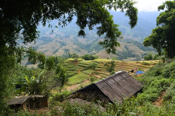 Fototapeta na wymiar Old house in small village in the mountains. Traditional vietnamese rural landscape with terraced rice fields. Valley vie on a background. Sa Pa, Vietnam
