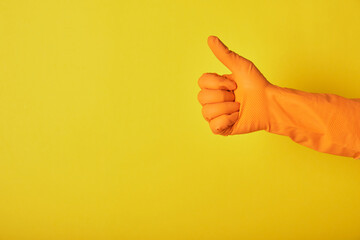 Hand in orange glove shows thumb up on a bright yellow background