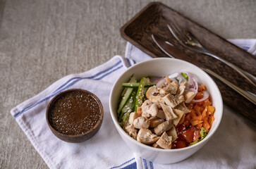 Fototapeta premium Healthy organic chicken Hawaiian poke bowl with cucumber, rice, carrots, onion served in bowl on table decorated with kitchen napkin. Healthy lifestyle