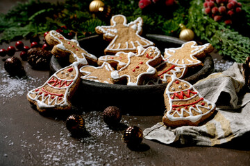 Homemade traditional Christmas gingerbread cookies with icing ornate. Gingerbread Man, angel, bell on ceramic plate with xmas decorations over dark background.