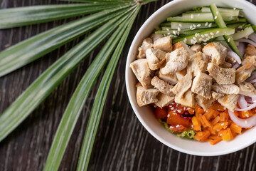 Healthy organic chicken poke bowl with cucumber, rice, carrots, onion served in bowl on wooden...