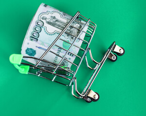 Russian rubles in a grocery basket on a green background. The cart fell. Fall of the ruble. Russian...