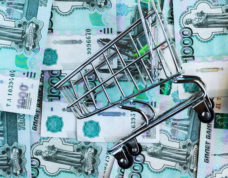 Russian Rubles Under An Empty Grocery Cart Against The Background Of 1000 Rubles Banknotes. View From Above. Selective Focus.