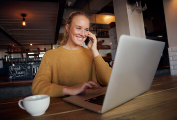 Portrait of smiling young business woman talking over smartphone and using laptop in cafe