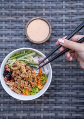 Close up of a hand with chopsticks and healthy organic vegetarian poke bowl with tofu, fermented...