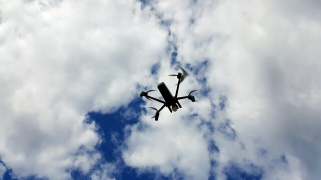 Controlled drone with mounted camera flies in cloudy blue sky.