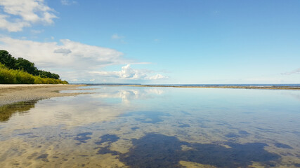 Calm sea on a sunny summer day. Blue cloudy sky and tree reflection in tranquil water. Holiday and travel concept. Latvian nature.
