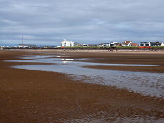 People walking on the beach at blundell sands in crosby near southport merseyside with building and liverpool docks in the distance