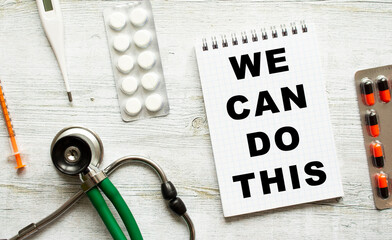 WE CAN DO THIS is written in a notebook on a white table next to pills and a stethoscope.