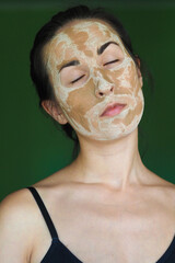 young brunette woman with a clay homemade mask on her face with her eyes closed