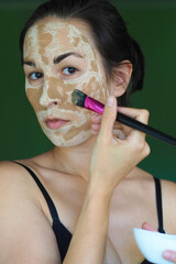 young brunette woman with a clay homemade mask on her face