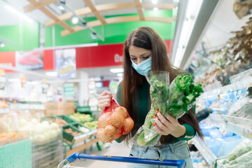 Young caucasian woman with long hair wearing a protective medical mask buys greens in a supermarket
