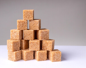 Brown cane sugar cubes stacked on top of each other. Sugar crystals. On a light gray background. Close-up.