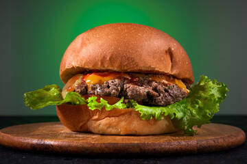 Burger on the wooden board on a green background. Tasty grilled home made burger with beef, tomato, cheese and cucumber.