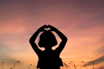 Child girl making heart symbol with her hands at sunset background