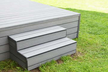 Part of dark gray or anthracite wpc composite material terrace deck with stairs  in backyard green grass outdoors.
