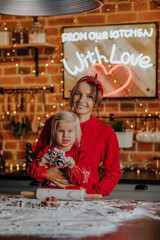 Woman posing with her blond girl in the kitchen against Christmas background.