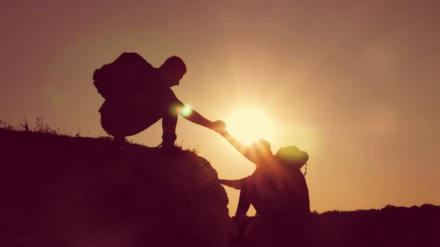 Silhouette of helping hand between two climber. two hikers on top of the mountain, a man helps a man to climb a sheer stone. couple hiking help each other silhouette in mountains with sunlight.