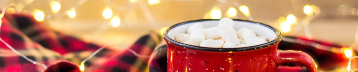 Banner of Red cup with hot coffee and sweet marshmallows with plaid in Christmas decorations with garland lights
