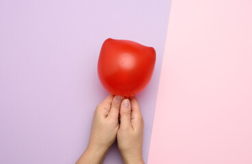female hand holding an inflated red air balloon on a pink background