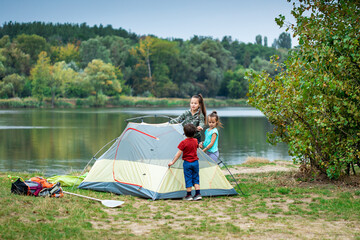 Three children pitching tent together near lake