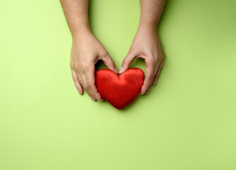 female hands holds red textile heart, green background